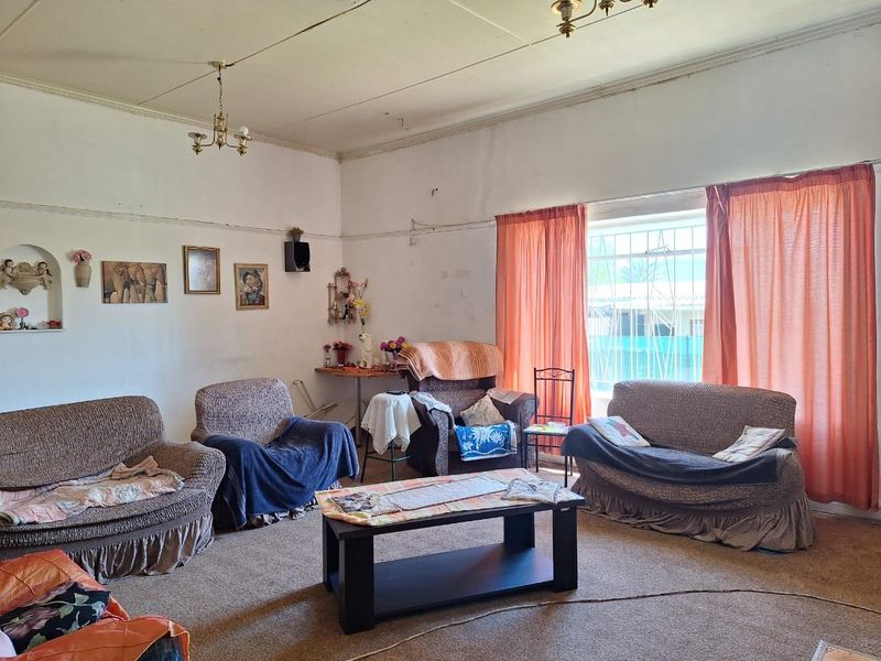 A living room featuring dated wall finishes, worn carpeting, and security bars on the window, offering potential for renovation and modernization.
