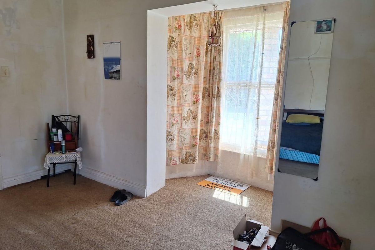 A bedroom featuring carpet flooring and a recessed window area, currently requiring wall repairs and cosmetic updates to improve its overall condition.
