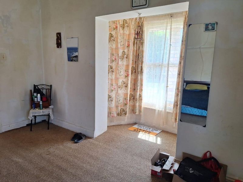 A bedroom featuring carpet flooring and a recessed window area, currently requiring wall repairs and cosmetic updates to improve its overall condition.