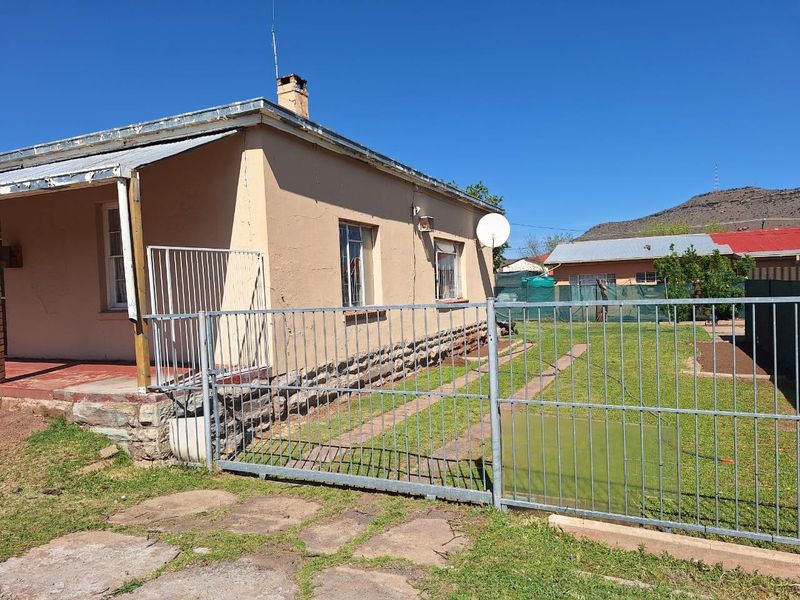 Rear view of the property featuring a covered patio, metal security fencing, and a stone foundation base.