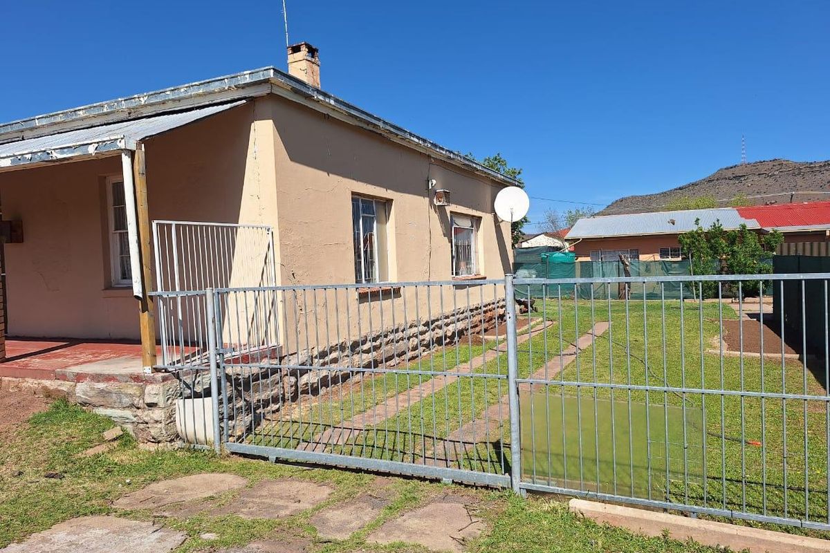 Rear view of the property featuring a covered patio, metal security fencing, and a stone foundation base.