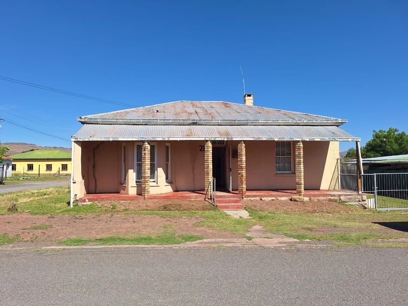 Front elevation of a single-story house featuring a corrugated iron roof, brick pillars, and a covered veranda, showing signs of significant exterior wear.