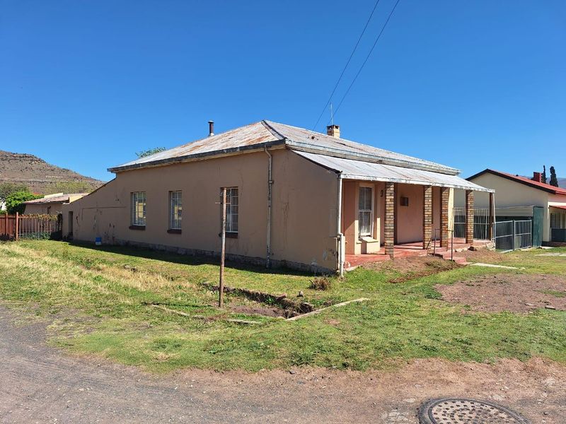Front view of a single-story house featuring a corrugated iron roof, covered veranda with brick pillars, and surrounding yard space.