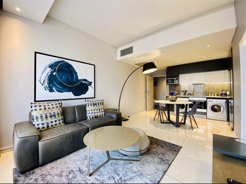 Modern open-plan living area featuring a sleek kitchen with built-in cabinetry, integrated appliances, and polished tiled flooring throughout.