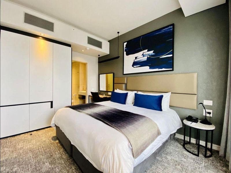 Modern bedroom featuring a built-in wardrobe, integrated ducted air conditioning, and an upholstered headboard with direct access to an en-suite bathroom.