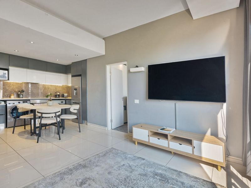 Modern open-plan living area featuring a sleek kitchen with built-in cabinetry, stone-look backsplash, and polished tiled flooring throughout.