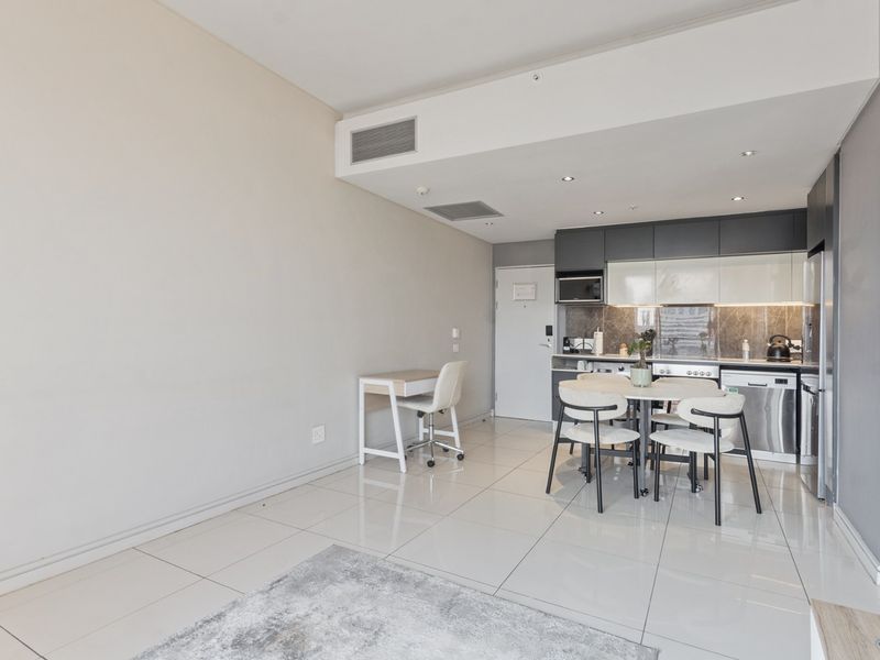Modern open-plan living area featuring a sleek kitchen with built-in appliances, high-gloss cabinetry, and polished tiled flooring throughout.