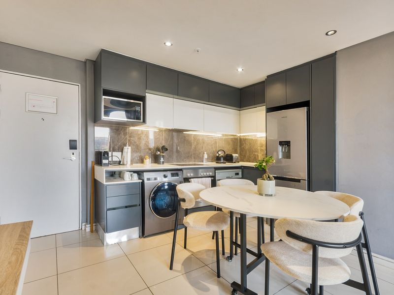 Modern open-plan kitchen featuring sleek two-tone cabinetry, stone-look backsplash, integrated appliances, and tiled flooring, seamlessly combined with a dining area.