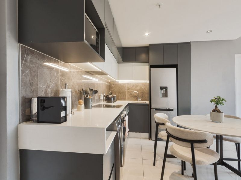 Modern open-plan kitchen featuring sleek dark and white cabinetry, quartz countertops, integrated appliances, and stylish under-cabinet lighting, seamlessly flowing into the dining area.