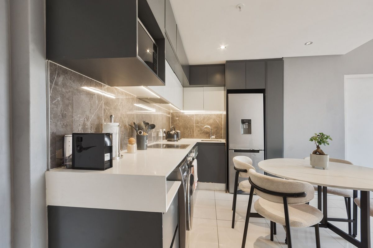 Modern open-plan kitchen featuring sleek dark and white cabinetry, quartz countertops, integrated appliances, and stylish under-cabinet lighting, seamlessly flowing into the dining area.