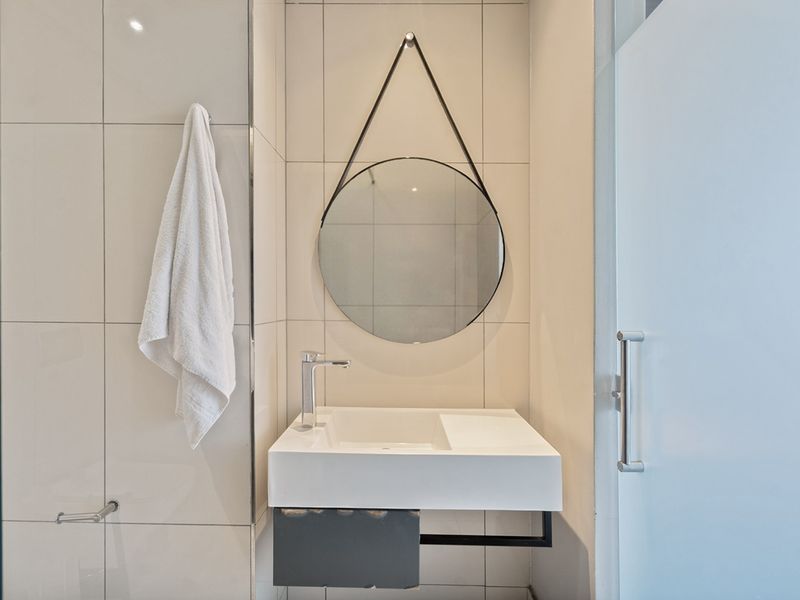 Modern bathroom featuring a wall-mounted basin with chrome mixer tap, tiled walls, and a glass shower screen.