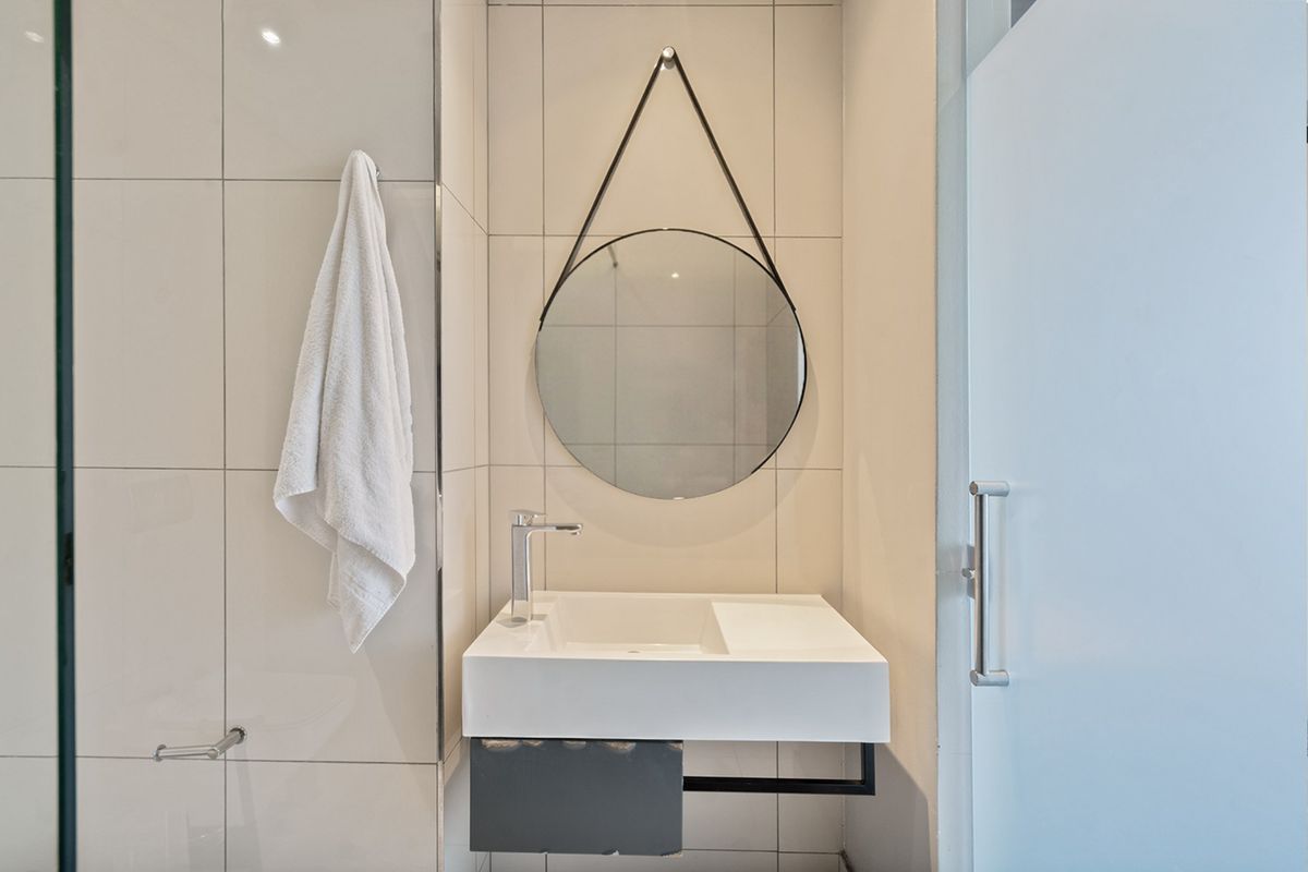Modern bathroom featuring a wall-mounted basin with chrome mixer tap, tiled walls, and a glass shower screen.
