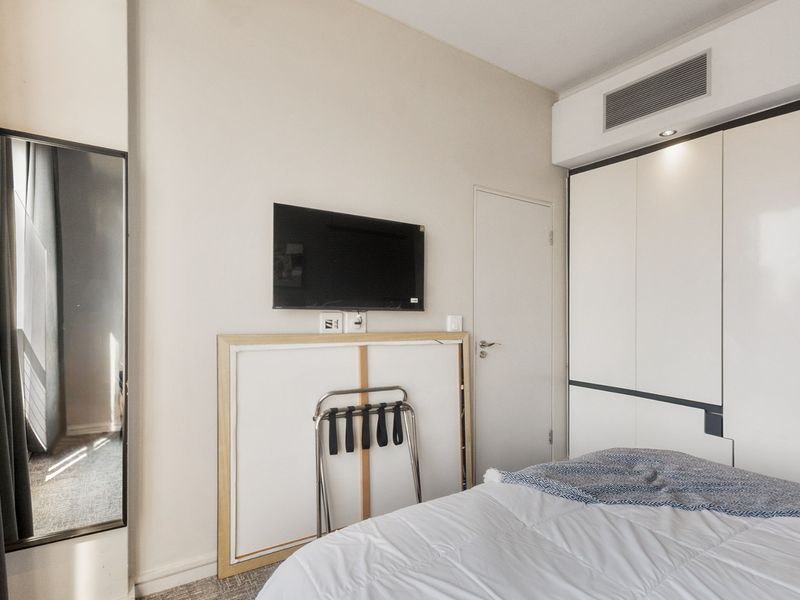 A modern bedroom featuring a built-in wardrobe, wall-mounted television, and integrated ducted air conditioning system.