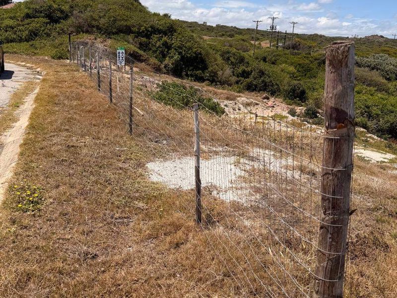 A view of the vacant residential land boundary featuring wire mesh fencing and wooden posts along the roadside.