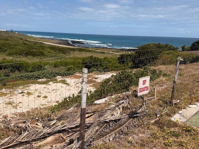 A view of the coastal landscape from the vacant residential property, featuring a wire fence and a deep excavation warning sign.