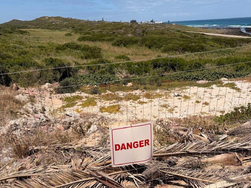 A view of the coastal landscape and natural terrain, featuring wire mesh fencing and a danger warning sign.