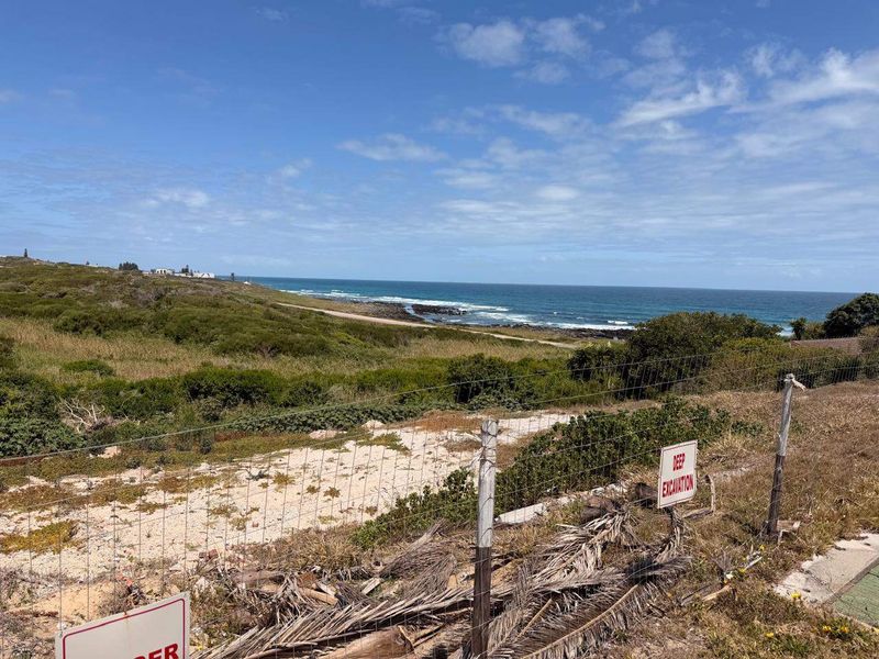 A scenic coastal view overlooking the ocean and natural landscape, featuring wire fencing and a marked deep excavation area on the property.