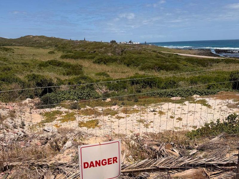 A coastal view overlooking undeveloped residential land with wire mesh fencing and a danger sign in the foreground.