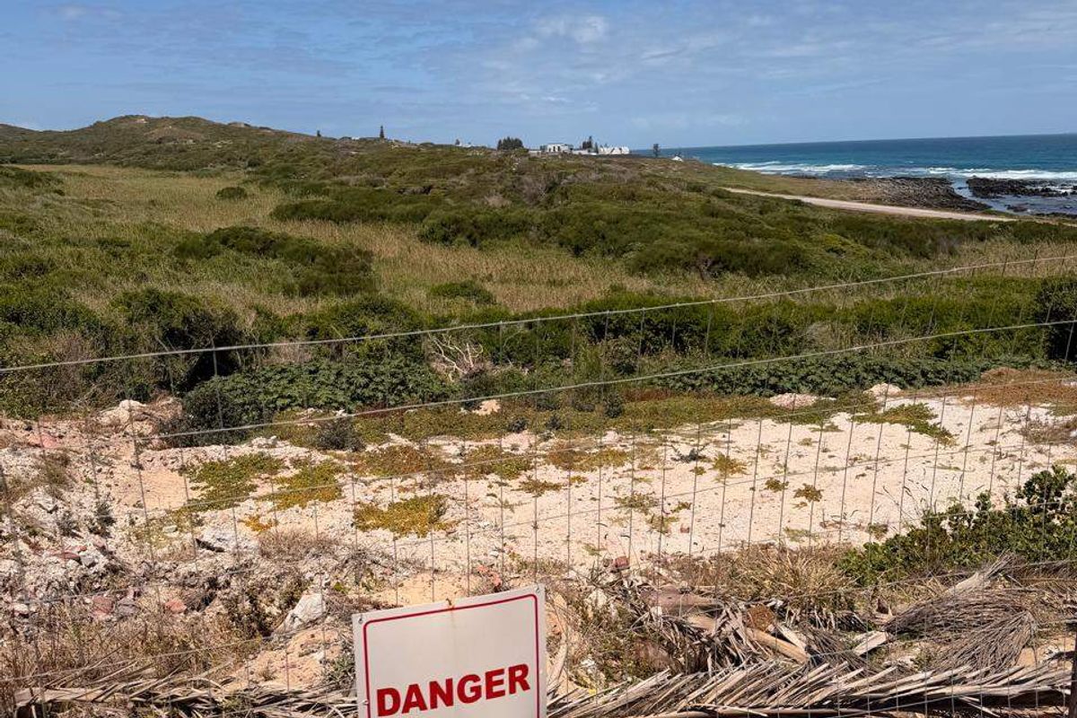 A coastal view overlooking undeveloped residential land with wire mesh fencing and a danger sign in the foreground.