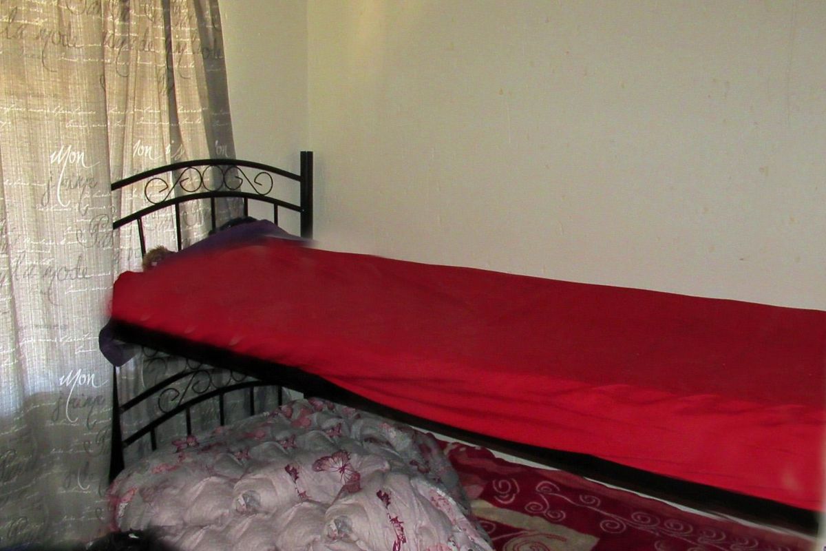 A bedroom space featuring plain walls and window treatments, currently showing signs of wear and surface imperfections.