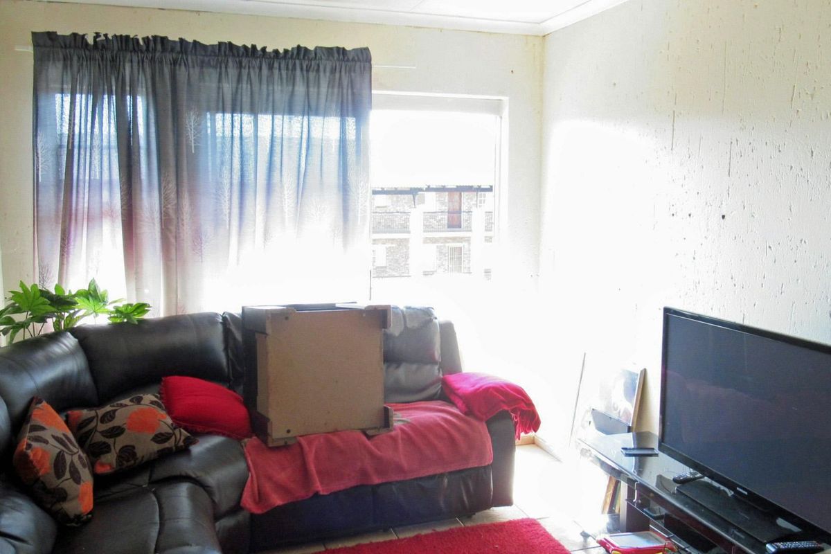 A living room area featuring tiled flooring and a large window, currently showing signs of wear on the wall surfaces.