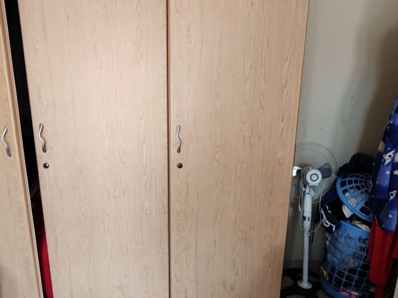 A bedroom featuring a light wood-finish built-in wardrobe with metal handles.