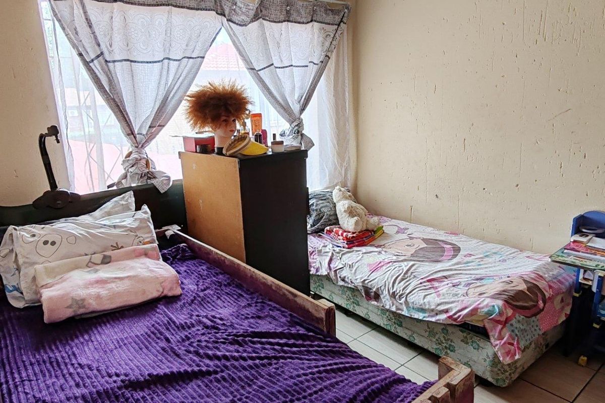 A bedroom featuring tiled flooring and a window, currently showing signs of wear on the wall surfaces.