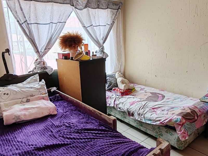 A bedroom featuring tiled flooring and a window, currently showing signs of wear on the wall surfaces.
