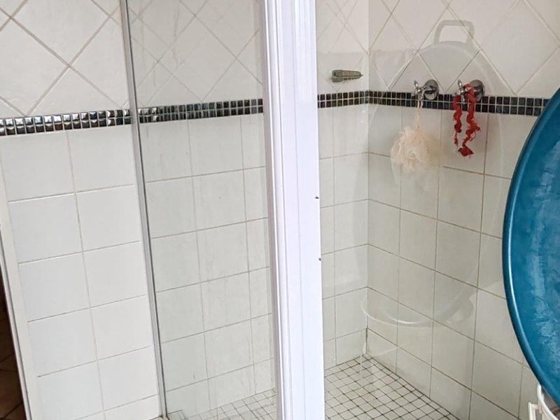 A functional bathroom shower enclosure featuring white tiled walls with a decorative border and tiled flooring.