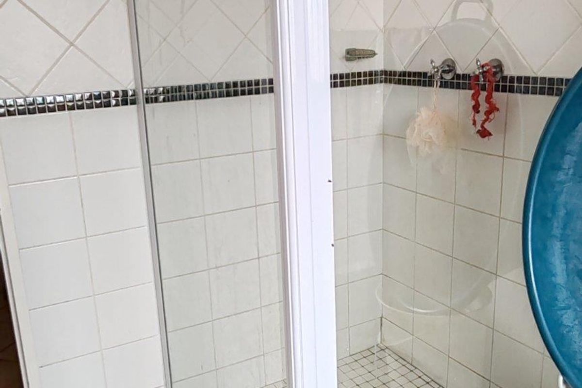 A functional bathroom shower enclosure featuring white tiled walls with a decorative border and tiled flooring.