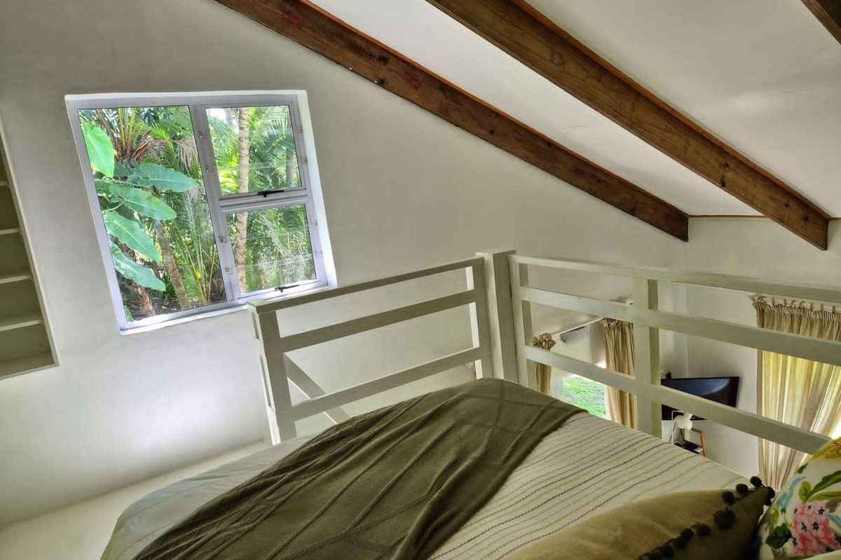 A cozy loft-style bedroom featuring exposed timber ceiling beams, built-in shelving, and a protective railing overlooking the lower level.