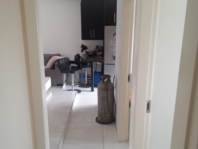 View from a hallway into an open-plan living and kitchen area featuring tiled flooring and modern dark cabinetry.