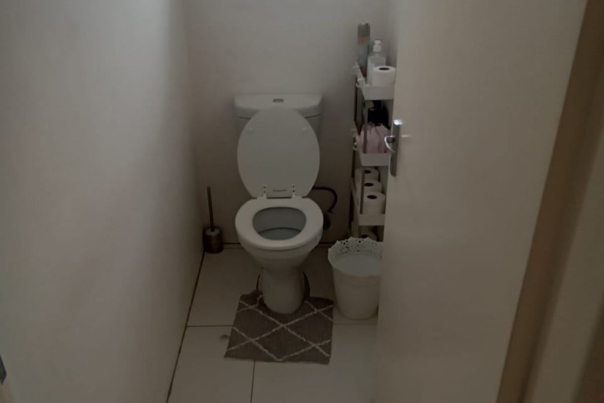 A compact guest toilet featuring tiled flooring and a small window with a security gate.