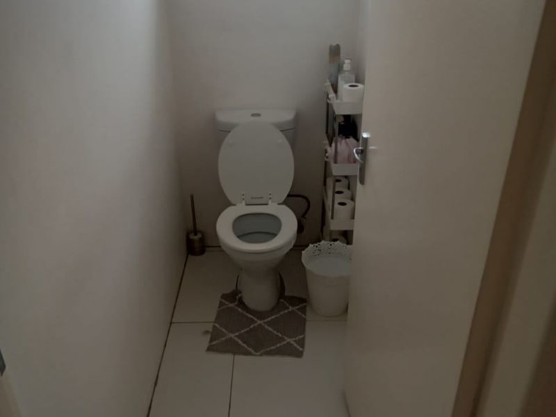A compact guest toilet featuring tiled flooring and a small window with a security gate.
