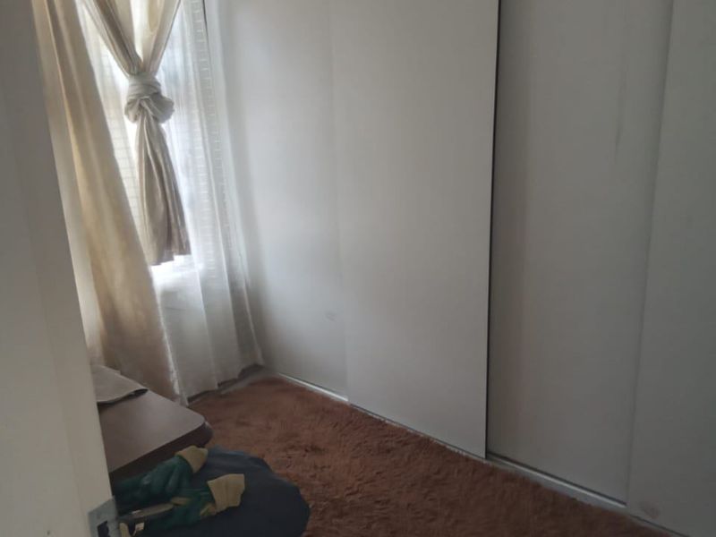 A compact bedroom featuring a built-in sliding door wardrobe and a window, providing a functional space with neutral finishes.