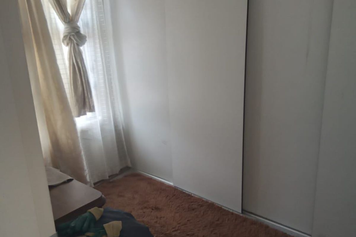 A compact bedroom featuring a built-in sliding door wardrobe and a window, providing a functional space with neutral finishes.