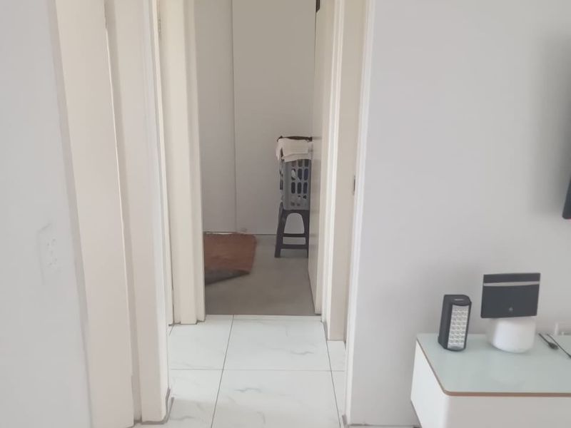 A bright, neutral hallway featuring white tiled flooring and multiple internal doorways leading to adjacent rooms.