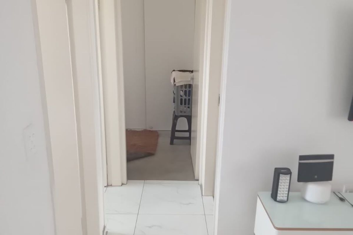 A bright, neutral hallway featuring white tiled flooring and multiple internal doorways leading to adjacent rooms.