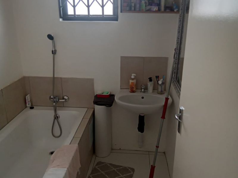 A functional bathroom featuring a bathtub with handheld shower attachment, a wall-mounted basin, and tiled finishes.