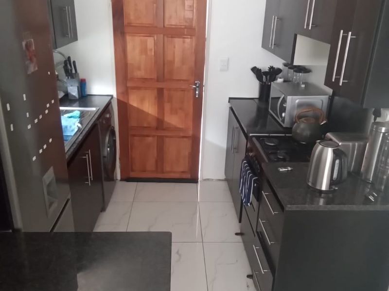A compact kitchen featuring dark cabinetry, granite countertops, built-in gas hob, oven, and tiled flooring, leading to a timber door.