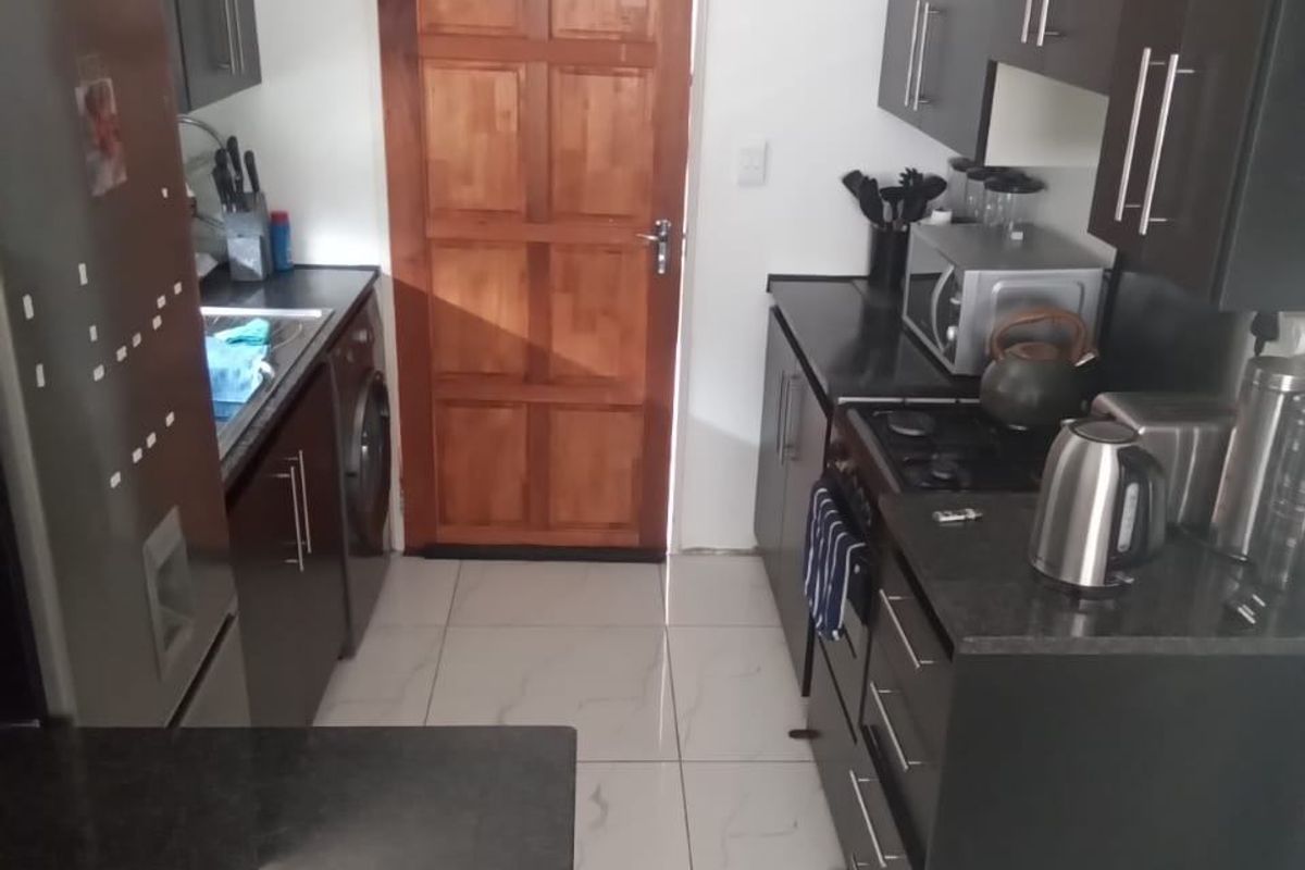 A compact kitchen featuring dark cabinetry, granite countertops, built-in gas hob, oven, and tiled flooring, leading to a timber door.