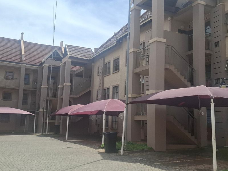 Exterior view of an apartment complex featuring paved parking areas with shade cloth carports and multi-level building access via external staircases.