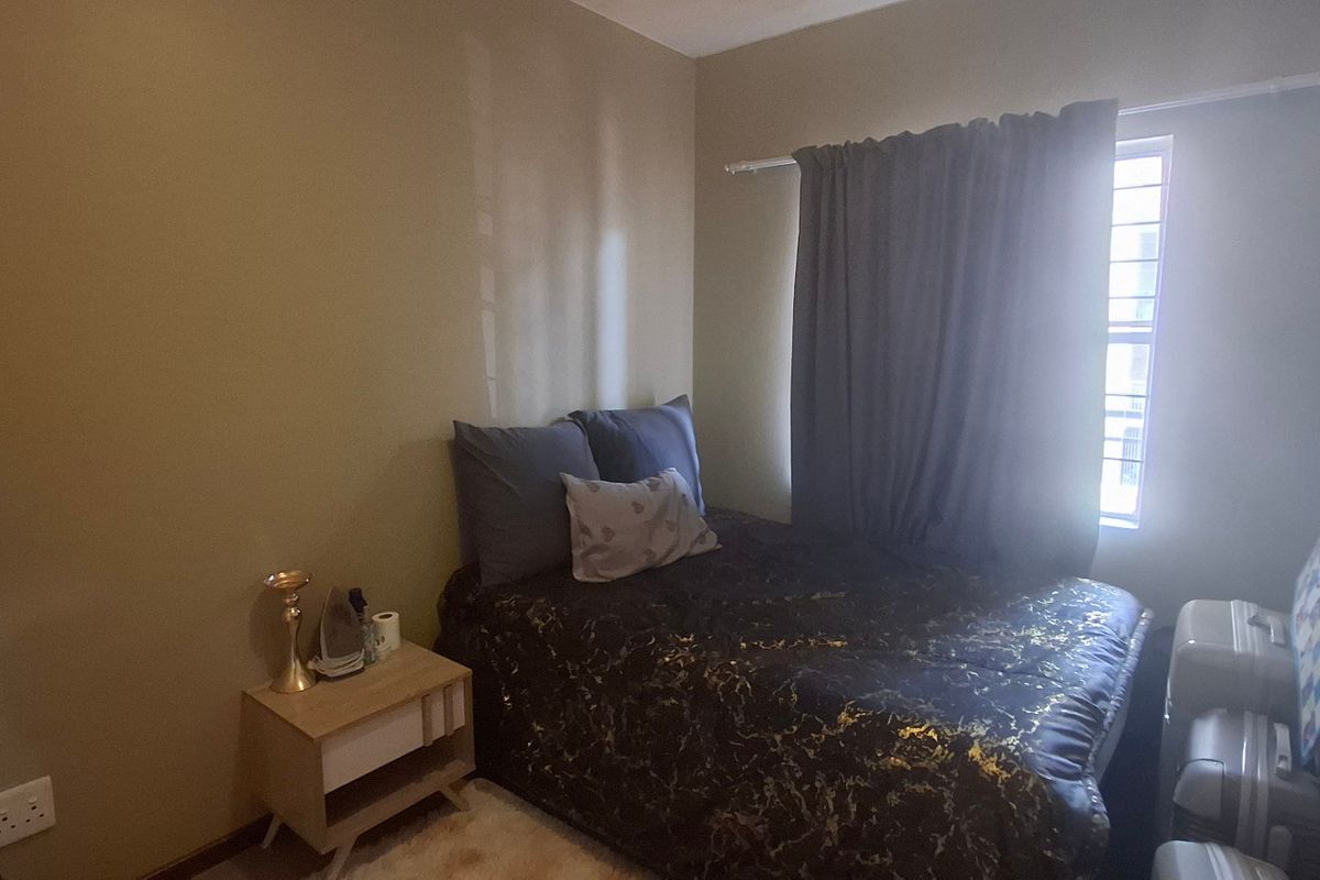 A compact bedroom featuring a window with security bars and neutral wall finishes, providing a functional sleeping space.