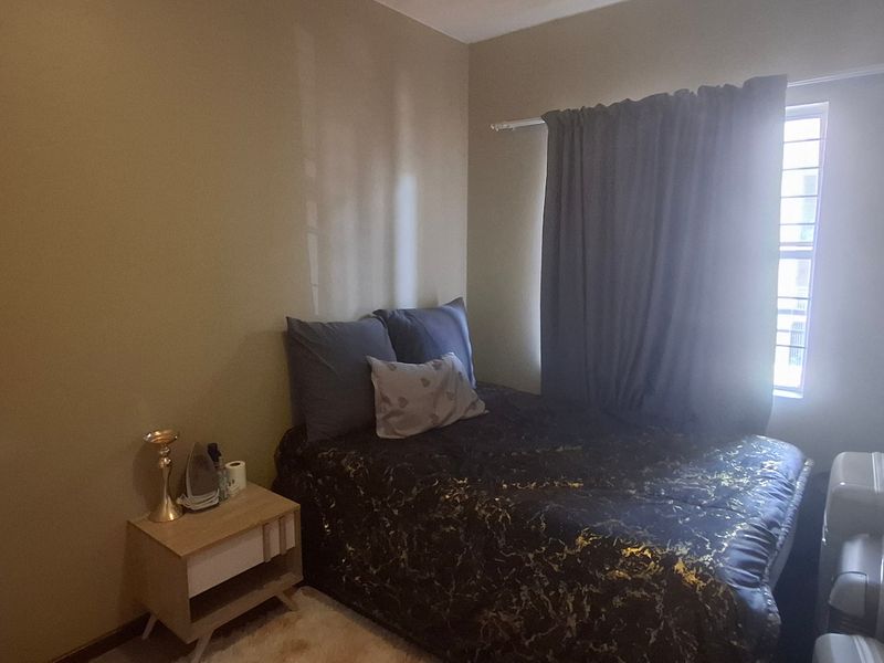 A compact bedroom featuring a window with security bars and neutral wall finishes, providing a functional sleeping space.