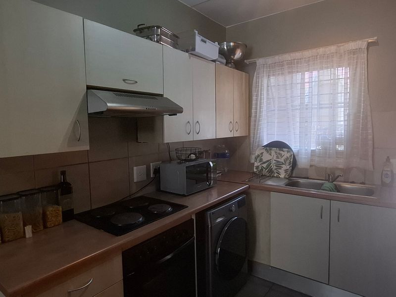 Compact kitchen featuring built-in cabinetry, electric hob, oven, extractor fan, and stainless steel sink with tiled backsplash and window security bars.