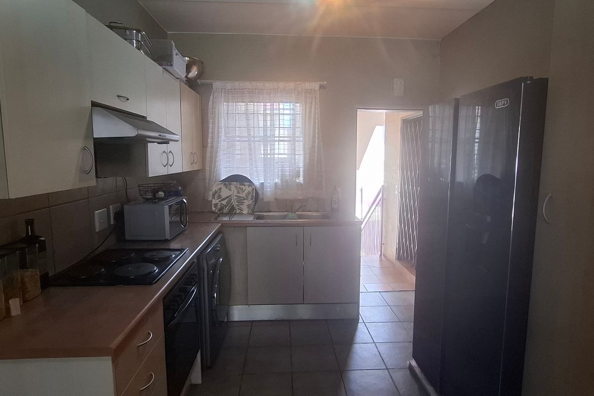 Functional kitchen featuring built-in cabinetry, laminate countertops, electric hob, oven, extractor fan, and tiled finishes with direct access to an exterior doorway.