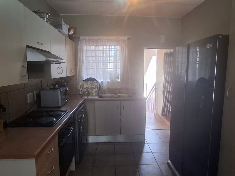 Functional kitchen featuring built-in cabinetry, laminate countertops, electric hob, oven, extractor fan, and tiled finishes with direct access to an exterior doorway.