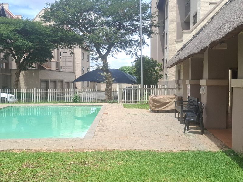 Communal outdoor area featuring a swimming pool, paved patio, and a covered thatched lapa for residents.