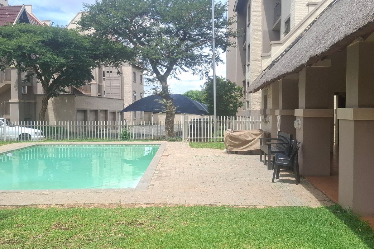 Communal outdoor area featuring a swimming pool, paved patio, and a covered thatched lapa for residents.