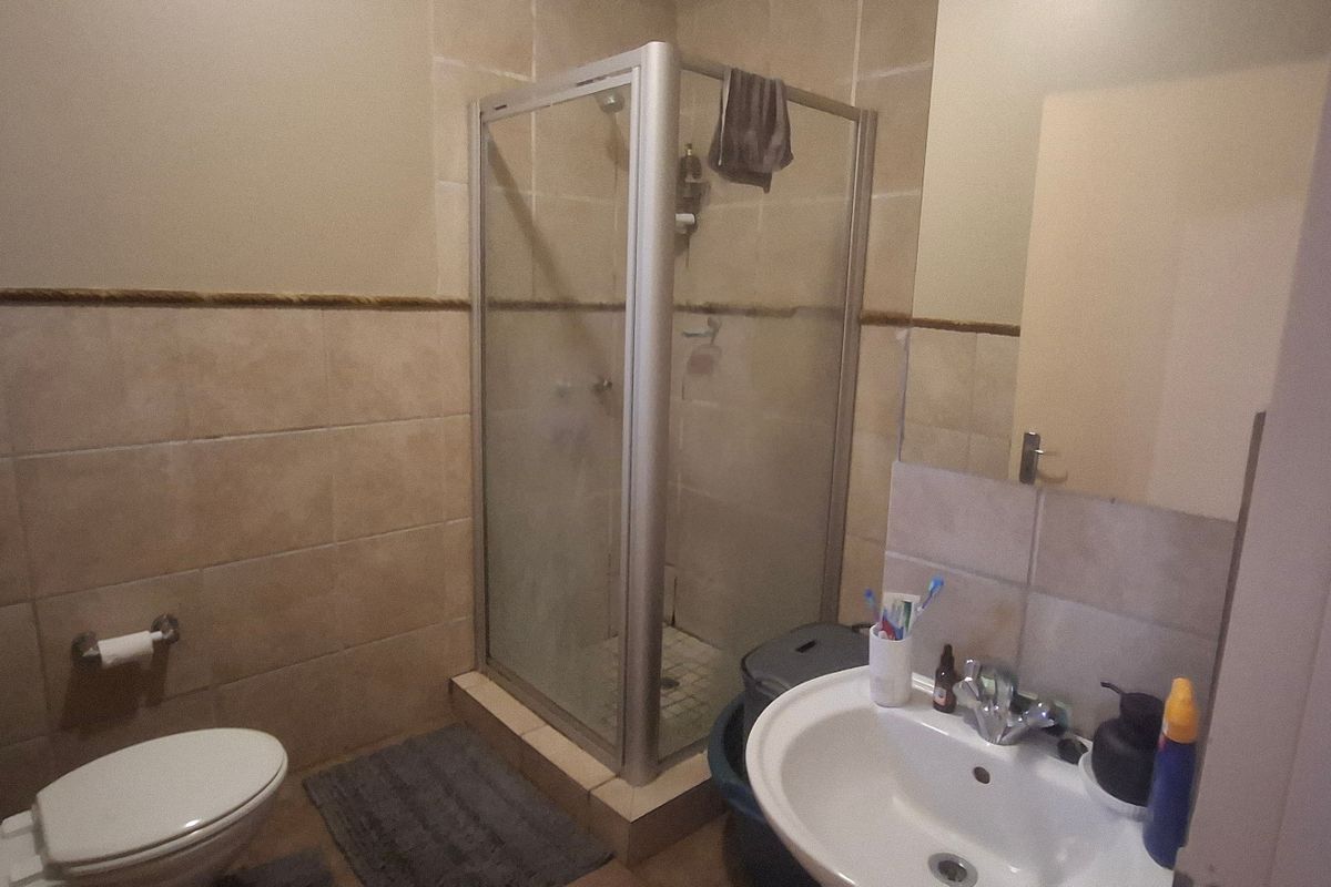 A functional bathroom featuring a shower enclosure, pedestal basin, and toilet with neutral wall tiling.